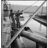 Chargement, à l'aide d'un palan, de torpilles dans les tubes lance-torpilles d'une tourelle orientable d'un sous-marin, à quai dans un port.
