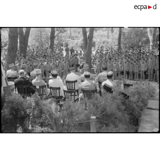 Vue d'ensemble des élèves de l'Ecole militaire préparatoire nord-africaine (EMPNA) d'Hammam Righa, qui se tiennent debout, face au général de corps d'armée Henry Martin et à des personnalités militaires et civiles, assis.