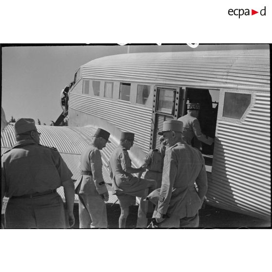 Le général de corps d'armée Henry Martin monte à bord d'un avion de transport, suivi par le général de division Jean Breuillac et des autorités militaires.