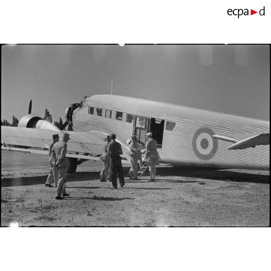 Le général de corps d'armée Henry Martin accède à un avion de transport, suivi par le général de division Jean Breuillac et des autorités militaires.