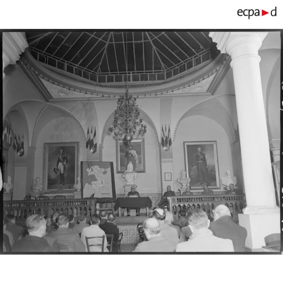 Une autorité militaire s'adresse à l'assemblée des officiers de réserve et utilise une carte géographique de l'Indochine pour illustrer ses propos.