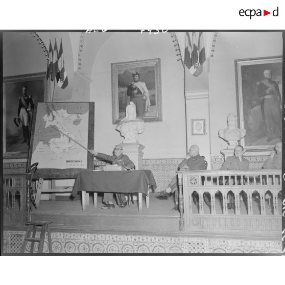 Une autorité militaire s'adresse à l'assemblée des officiers de réserve et utilise une carte géographique de l'Indochine pour illustrer ses propos.