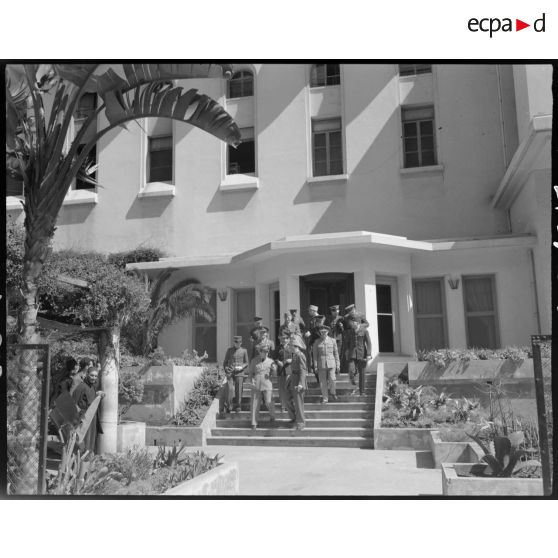 Un groupe d'attachés et de chefs de missions militaires étrangers descendent les escaliers extérieurs de l'entrée principale d'un bâtiment.