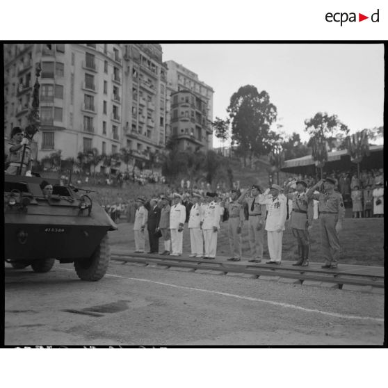 Le général de brigade Jean Breuillac assiste à un défilé motorisé, accompagné d'autorités militaires, sous le regard de la population civile.