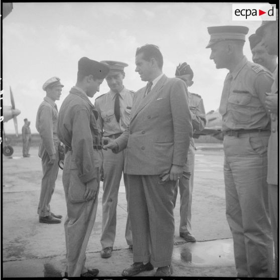 Edmond Michelet, ministre des Armées, s'entretient avec un soldat, accompagné d'autorités militaires, sur une base aérienne.