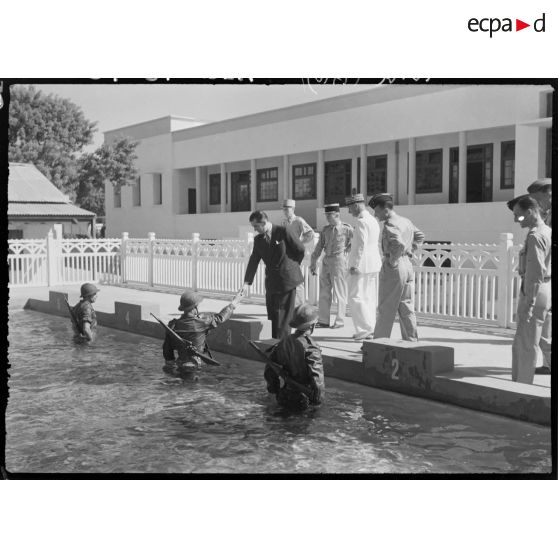 Edmond Michelet, ministre des Armées, accompagné d'autorités militaires, s'entretient avec des militaires en entrainement dans une piscine.