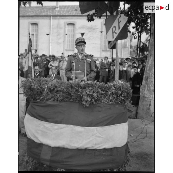 Une autorité militaire prononce un discours, sous le regard d'autorités civiles, militaires et de la population civile.