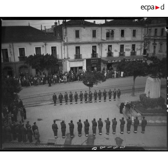 Plan en plongée d'une cérémonie militaire devant le monument aux morts de Maison Carrée, sous le regard de la population civile.