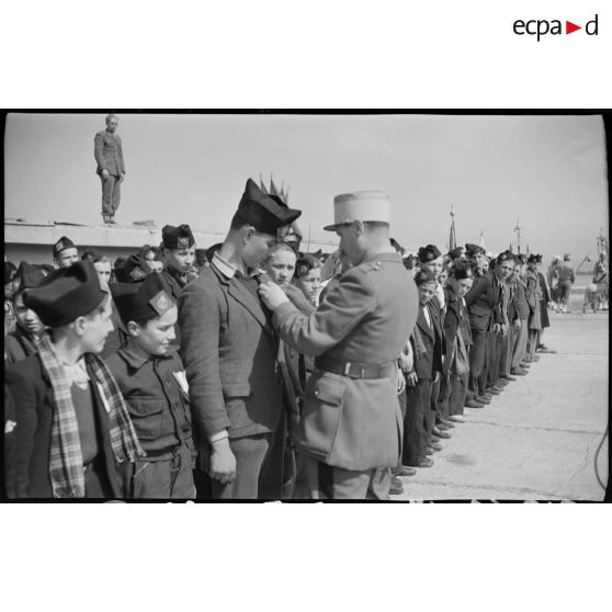 Une personnalité militaire remet une décoration à un jeune garçon originaire de Saint-Etienne, sur le port d'Alger.