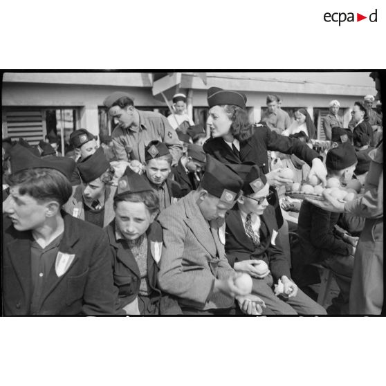 Une femme militaire distribue des oranges à de jeunes gens originaires de Saint-Etienne, arrivés au port d'Alger.
