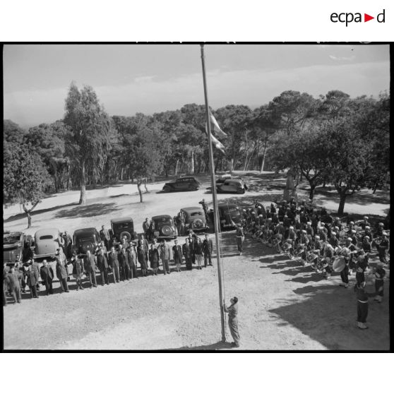 Plan en contre-plongée du lever de drapeau, sous le regard d'autorités civiles et militaires.