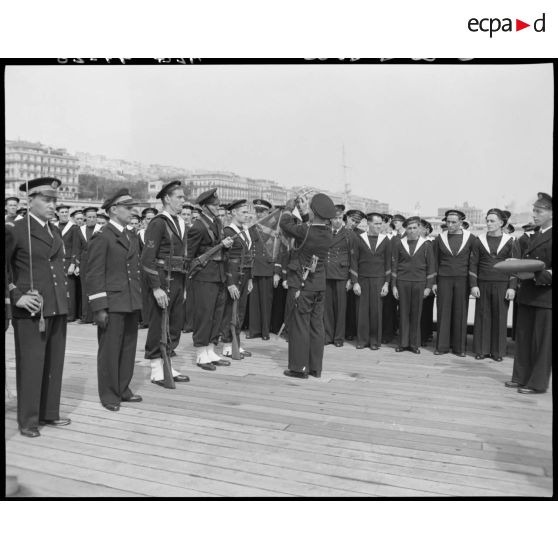 Cérémonie de remise de la croix de guerre à la compagnie de débarquement du croiseur Suffren, à quai, dans le port d'Alger : décoration de drapeau.