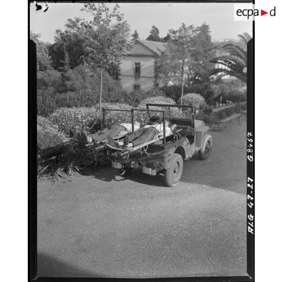 Deux hommes sont allongés sur deux brancards fixés à l'arrière d'une voiture Jeep transformée en transport sanitaire.