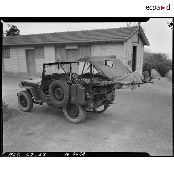 Deux hommes sont allongés sur deux brancards habrités par une bâche, fixés à l'arrière d'une voiture Jeep transformée en transport sanitaire.