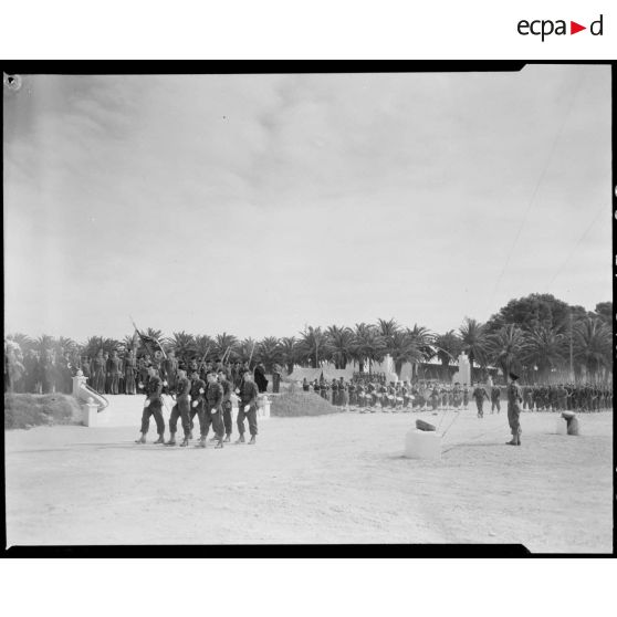 Défilé d'une unité militaire, sous le regard d'autorités civiles et militaires.