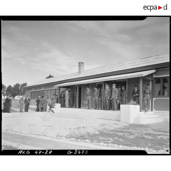Des personnalités civiles et militaires, parmi lesquelles le général Duché, se réunissent à l'intérieur d'un bâtiment militaire, sur le camp de Beni-Messous.