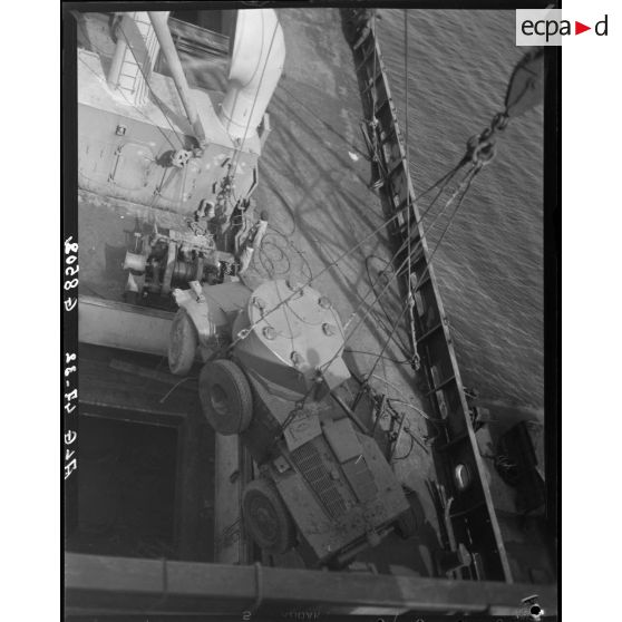 Plan en plongée du débarquement d'un véhicule militaire à l'aide d'une grue portuaire.