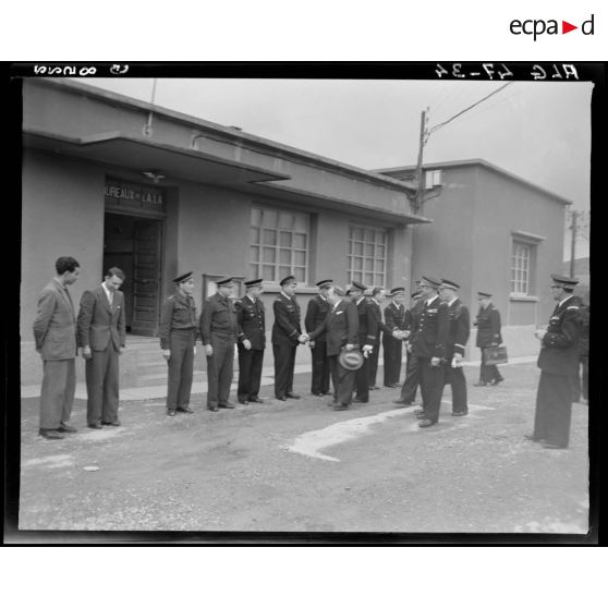 Le ministre de l'Air André Maroselli salue des autorirés militaires, devant un bâtiment administratif.