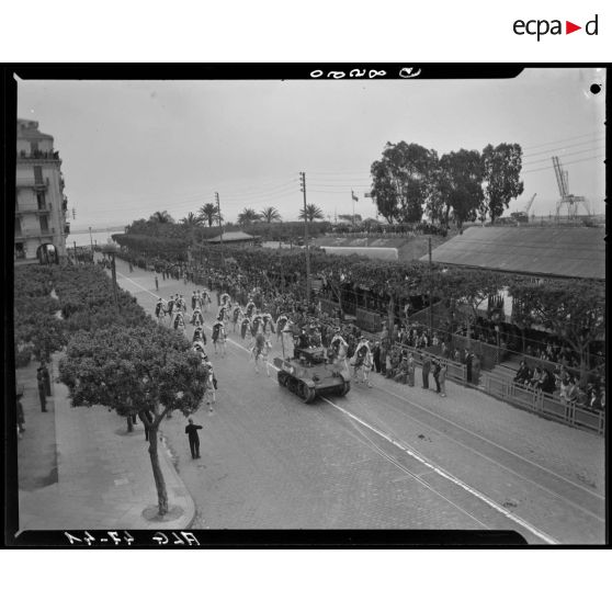 Plan en plongée du général Schlesser qui défile dans un char, suivi d'une unité de spahis, sous le regard d'autorités civiles et militaires.