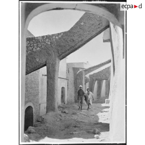 Vue d'une ruelle avec un passage voûté, à l'intérieur d'une enceinte, où se promènent deux jeunes garçons.