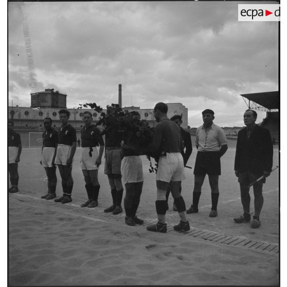 Le capitaine d'une équipe de football remet une gerbe au capitaine de l'équipe adverse.