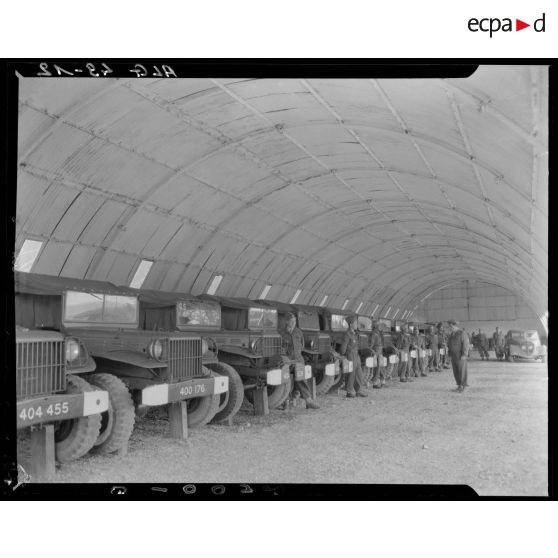 Plan d'ensemble d'un hangar où sont garés des camions militaires légers (Dodge).