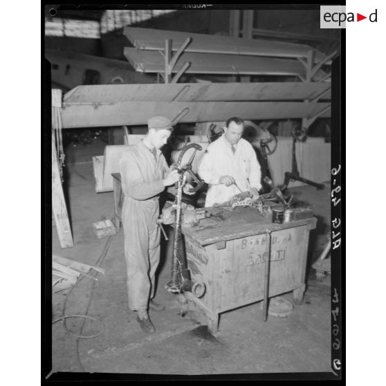Deux hommes travaillent sur des pièces de Toucan, dans un atelier d'aviation à Blida.