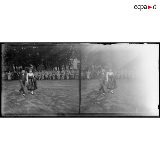 [Un jeune garçon et une jeune fille dansent, sous le regard d'autorités civiles et militaires.]