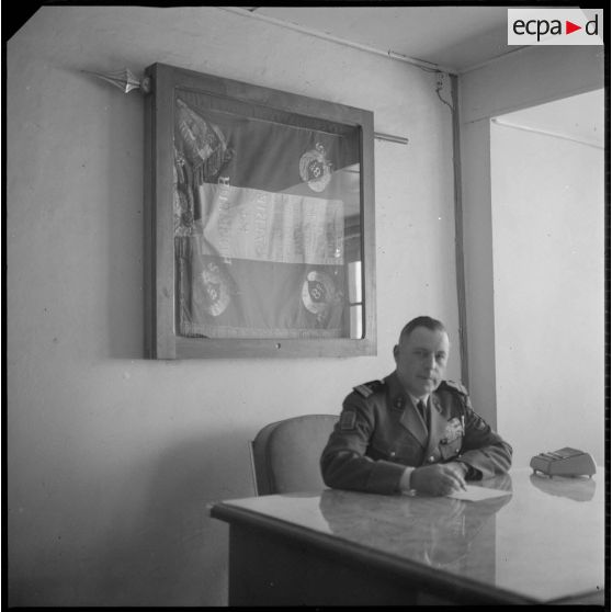 Portrait du colonel Alexandre, commandant le 8e RIM. Celui-ci est installé derrière son bureau, certainement au Camp des chasseurs. Au second plan, accroché au mur, le drapeau du 8e RIM. [légende d'origine]