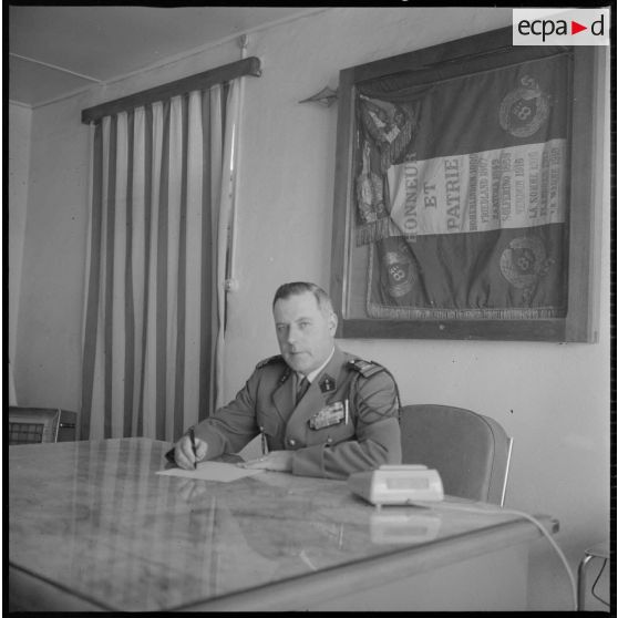 Portrait du colonel Alexandre, commandant le 8e RIM. Celui-ci est installé derrière son bureau, certainement au Camp des chasseurs. Au second plan, accroché au mur, le drapeau du 8e RIM. [légende d'origine]