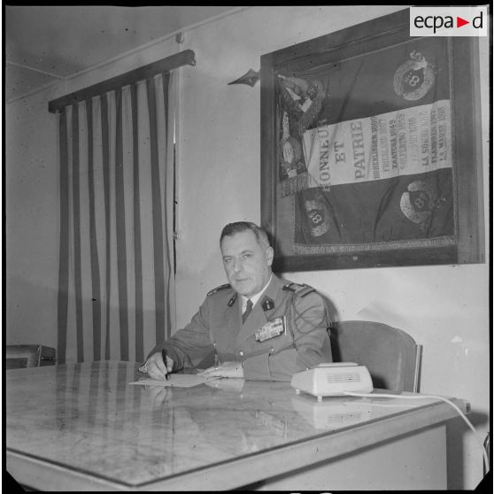 Portrait du colonel Alexandre, commandant le 8e RIM. Celui-ci est installé derrière son bureau, certainement au Camp des chasseurs. Au second plan, accroché au mur, le drapeau du 8e RIM. [légende d'origine]