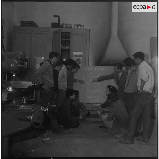 Apprentissage professionnel. Un enseignant explique à un groupe d'élèves un schéma d'assemblage reporté sur un tableau noir. [légende d'origine]