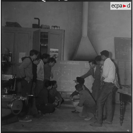 Apprentissage professionnel. Un enseignant explique à un groupe d'élèves un schéma d'assemblage reporté sur un tableau noir. [légende d'origine]