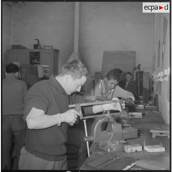 Apprentissage professionnel. A l'aide d'une scie à métaux, des élèves travaillent des pièces métalliques bloquées dans des étaux. [légende d'origine]