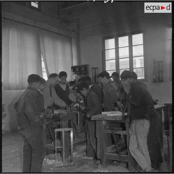 Apprentissage professionnel. Dans un atelier dédié au travail du bois, un groupe d'élèves écoute les explications de leur professeur. [légende d'origine]