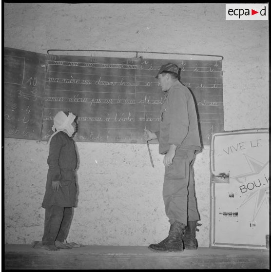 Apprentissage de la lecture. Sous la conduite d'un instituteur militaire, un jeune écolier lit les phrases reportées sur le tableau de la classe. [légende d'origine]