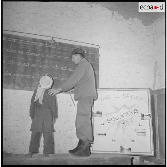 Apprentissage de la lecture. Sous la conduite d'un instituteur militaire, un jeune écolier lit les phrases reportées sur le tableau de la classe. [légende d'origine]