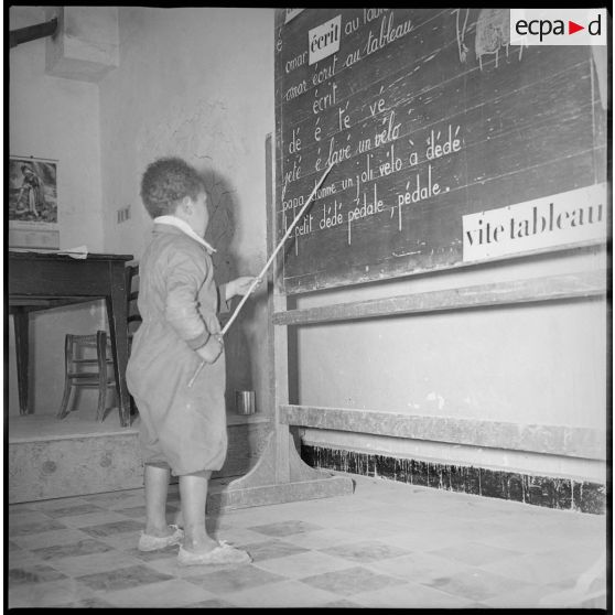 Un jeune écolier lit les phrases inscrites au tableau de sa classe. [légende d'origine]