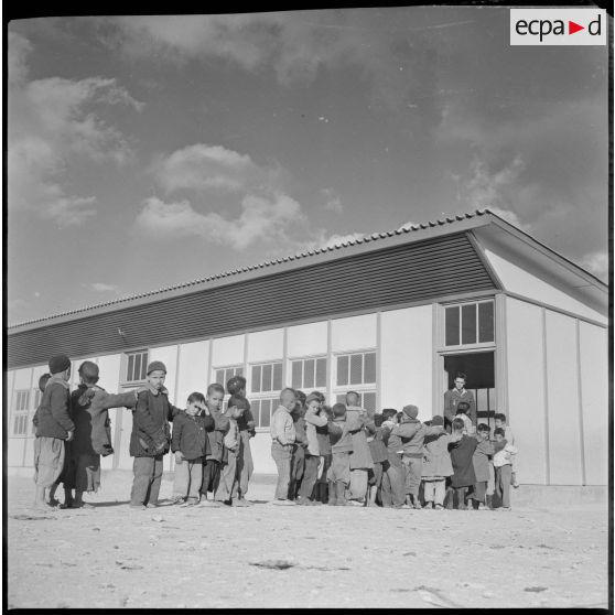 Jeunes écoliers en rang devant l'entrée de leur salle de classe. [légende d'origine]
