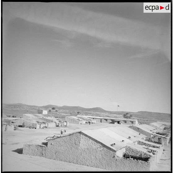 Vue du nouveau village du secteur de Berthelot. En arrière-plan, derrière le poteau au sommet duquel flotte un drapeau, l'école du village. [légende d'origine]