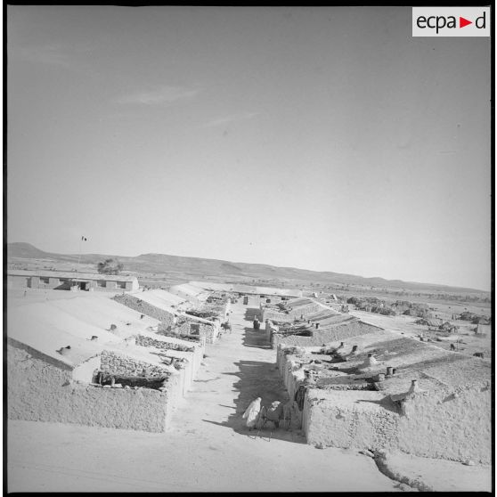 Vue du nouveau village du secteur de Berthelot. En arrière-plan, derrière le poteau au sommet duquel flotte un drapeau, l'école du village. [légende d'origine]