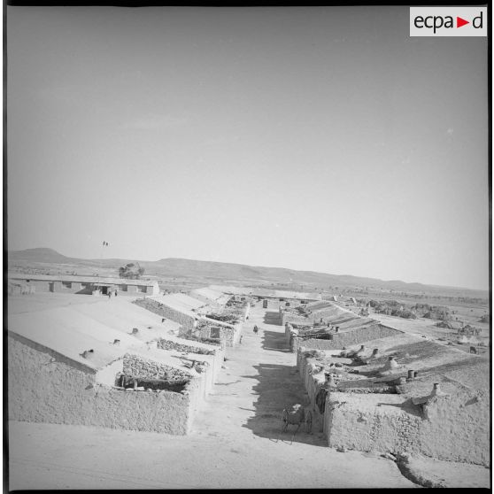 Vue du nouveau village du secteur de Berthelot. En arrière-plan, derrière le poteau au sommet duquel flotte un drapeau, l'école du village. [légende d'origine]