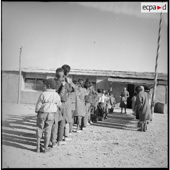 Des écoliers attendent en rang devant l'entrée de leur salle de classe. [légende d'origine]