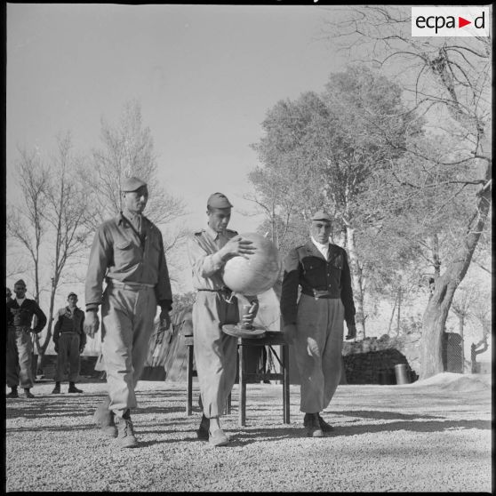 Leçon de géographie au commando Cobra. Encadré par deux de ses camarades, un membre du commando Cobra transporte un globe terrestre. [légende d'origine]