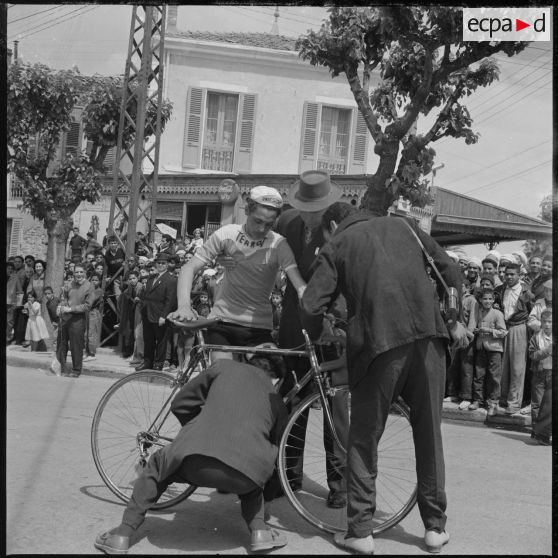 Course cycliste à Saïda. Un cycliste est à l'arrêt et des hommes s'affairent autour de son vélo. [légende d'origine]