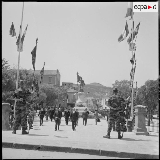 Visite de Paul Delouvrier. Le Délégué général du gouvernement en Algérie Paul Delouvrier passe devant le monument aux morts de Saïda et se dirige vers l'hôtel de ville. Au premier plan, des membres représentants des commandos de chasse du secteur (le nom des sticks est inscrit sur les fanions). [légende d'origine]