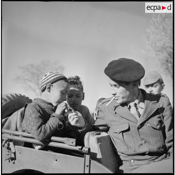 [Un soldat allume la cigarette d'un jeune garçon du village.]