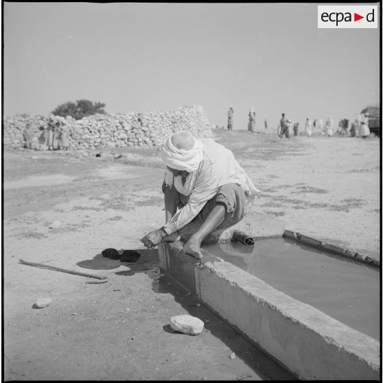 Visite d'un village. Un homme se lave les pieds à un point d'eau. [légende d'origine]