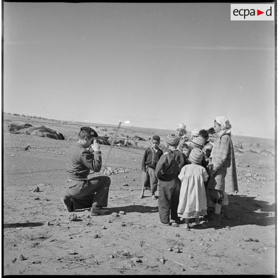 Un soldat photographie un groupe d'enfants du village. En arrière-plan, on distingue plusieurs khaïmas. [légende d'origine]