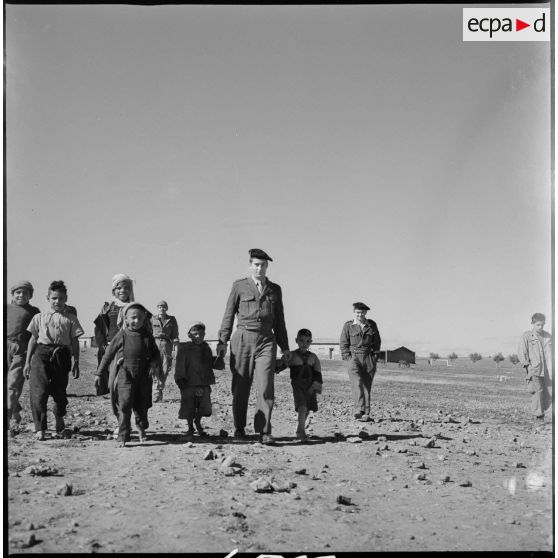 Un soldat et des enfants du village marchent main dans la main. [légende d'origine]